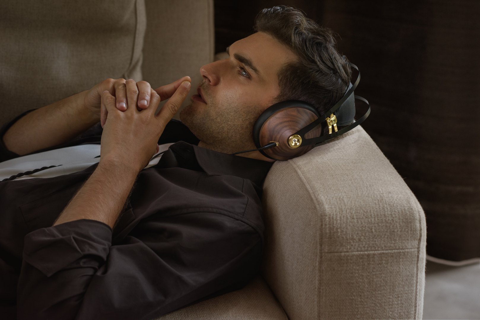 A lifestyle photo of a young person wearing Meze Audio 99 Classic Gen2 headphones while lying on a sofa