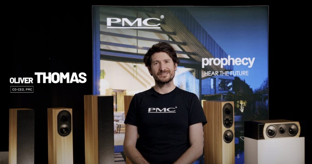Uus PMC kõlarite kaasjuht esitlusbänneri ees, mis tutvustab uut Prophecy-seeria transmission-line tehnoloogiaga kõlarit.