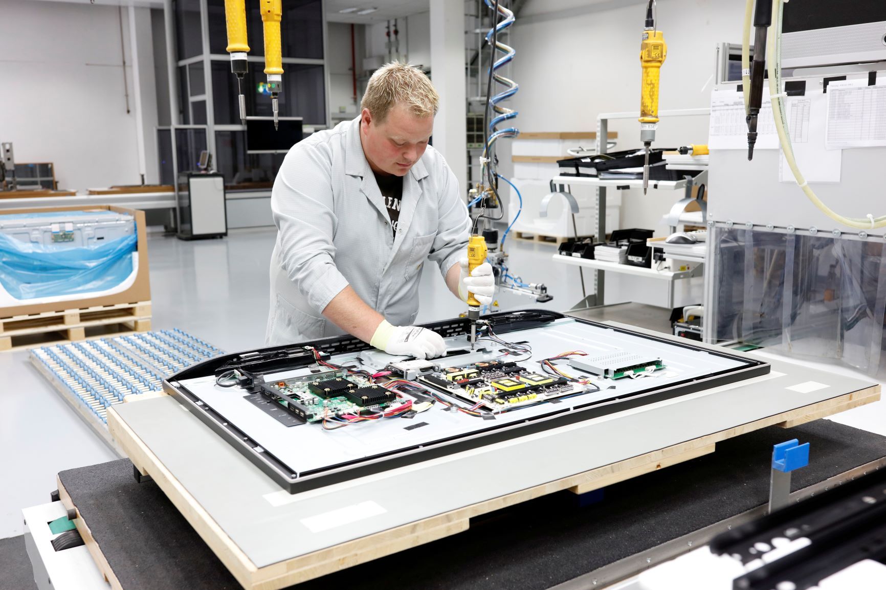 An assembly worker uses tools to mount circuit boards on an OLED TV at Loewe's factory in Kronach, Germany