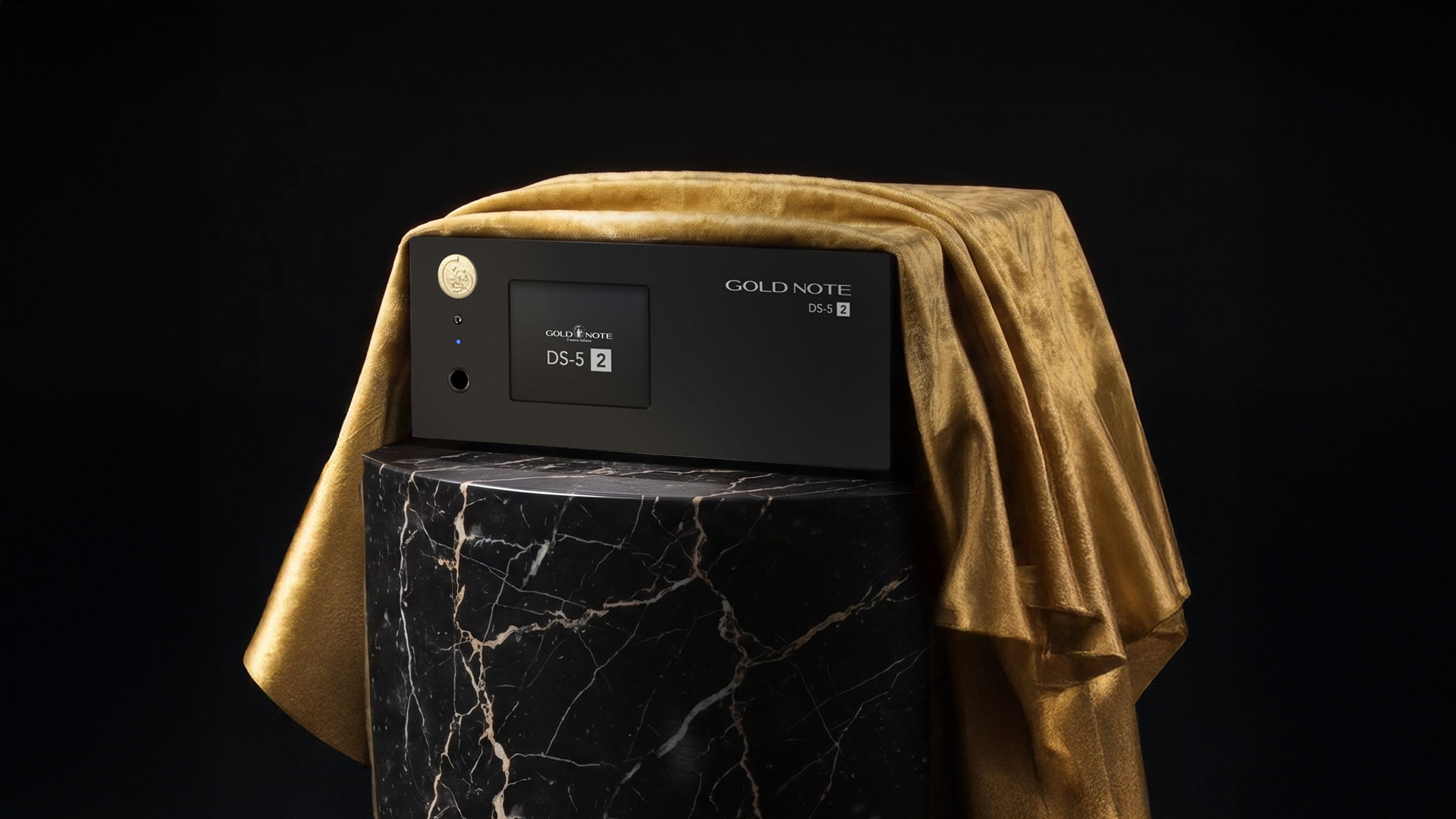 A staged reveal photoshoot with the new Gold Note DS-5.2 music streamer draped with a golden cloth and positioned on a marble pedestal