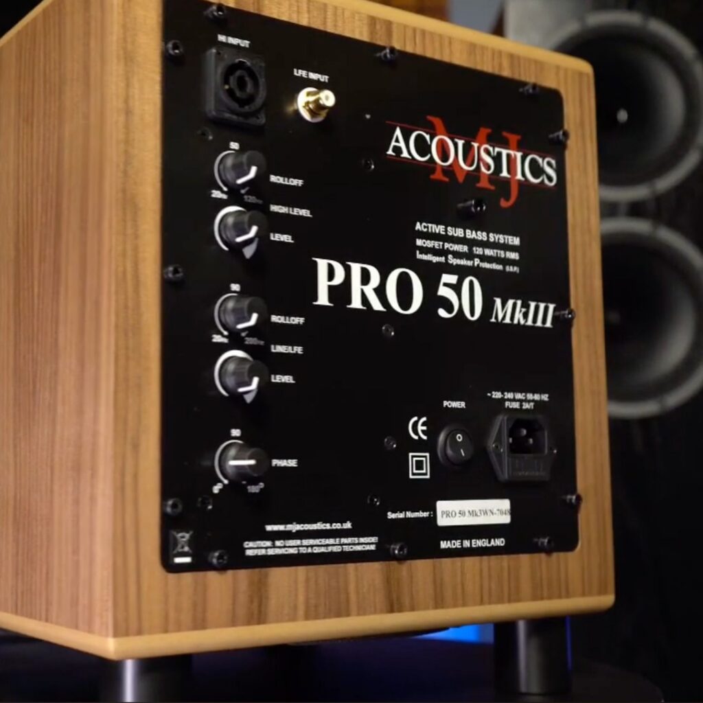 Black control panel on a wooden speaker cabinet labeled Acoustics Pro 50 MkIII with multiple knobs (Level, Drive, etc.) and input/output connectors visible. Made in England.